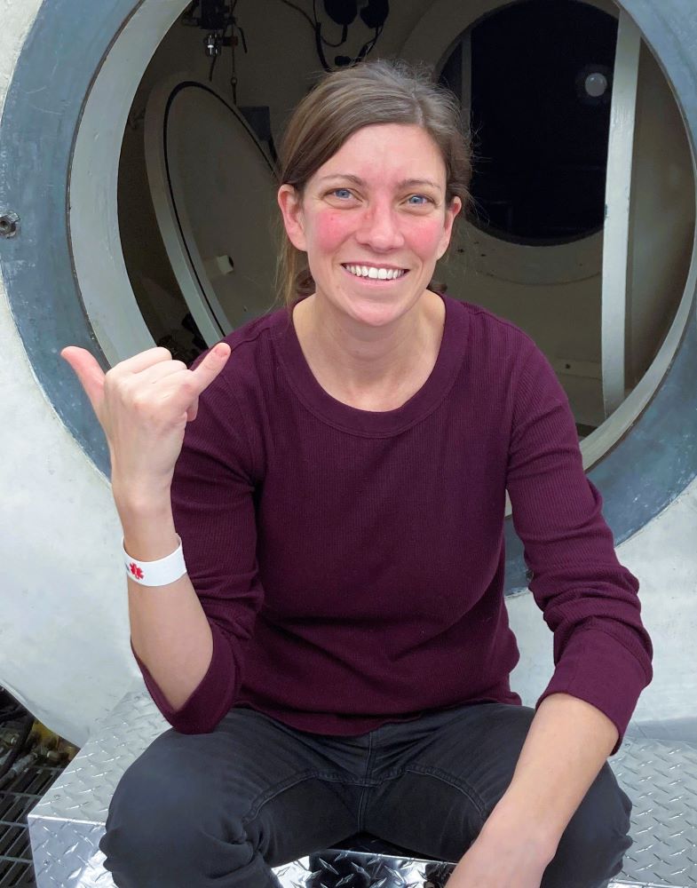 Tonya Ste. Marie fait le geste d'un symbole de la main 'hang loose' alors qu'elle est assise sur les marches d'un avion.