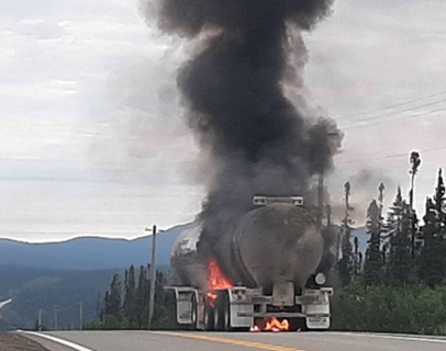 Truck on the side of the road with a fire coming from the rear tires and presence of black smoke. 